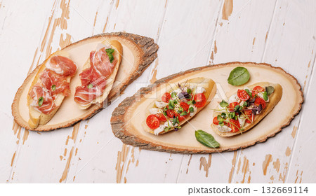 Tasty antipasto toasts featuring classic caprese with mozzarella and tomatoes, and savory prosciutto with herbs 132669114