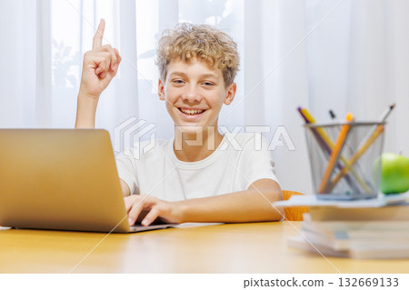 Schoolboy studying at home with laptop, notebook, and learning materials, smiling happily Schoolboy studying at home with laptop, notebook, and learning materials, smiling happily 132669133