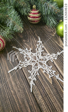 A white crocheted snowflake-shaped doily with fir branches and decorations. A white crocheted snowflake-shaped doily with fir branches and decorations. 132669619