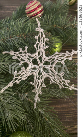 A white crocheted snowflake-shaped doily with fir branches and decorations. A white crocheted snowflake-shaped doily with fir branches and decorations. 132669622