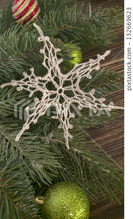 A white crocheted snowflake-shaped doily with fir branches and decorations. A white crocheted snowflake-shaped doily with fir branches and decorations. 132669623