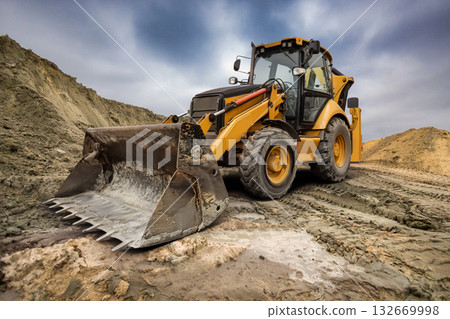 A heavy excavator loader moves dirt and rocks at a busy construction site, showcasing the power of modern engineering under a moody sky. A heavy excavator loader moves dirt and rocks at a busy construction site, showcasing the power of modern engineering under a moody sky. 132669998