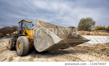 A large loader shifts dirt and gravel at a construction site, showcasing the power of machinery as clouds gather overhead on a cool afternoon A large loader shifts dirt and gravel at a construction site, showcasing the power of machinery as clouds gather overhead on a cool afternoon 132670007