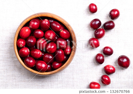 Fresh cranberries, bearberries, or American cranberries, in a wooden bowl, on linen. Ripe, bright red, large cranberries, Vaccinium macrocarpon, with shiny skin and acidic taste. Close-up, from above. Fresh cranberries, bearberries, or American cranberries, in a wooden bowl, on linen. Ripe, bright red, large cranberries, Vaccinium macrocarpon, with shiny skin and acidic taste. Close-up, from above. 132670766
