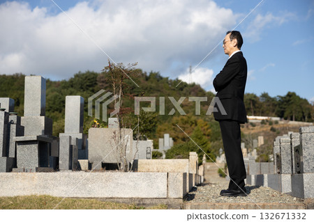 A middle-aged man wearing mourning clothes standing in a cemetery A middle-aged man wearing mourning clothes standing in a cemetery 132671332