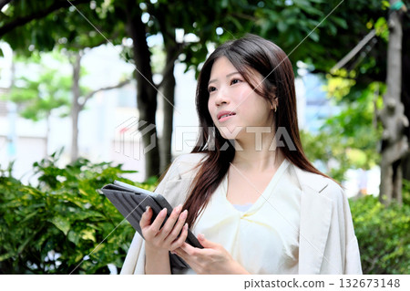 一位年輕的女商人正在公園的綠蔭下使用平板電腦。 132673148