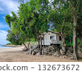 Secluded White Beach Hut or Wooden Cabin on Sand and Rocks, Surrounded by Lush Green Trees on a Tropical Island 132673672
