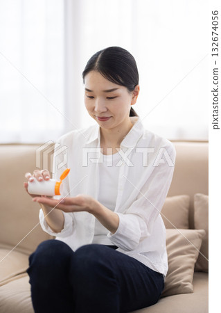 A middle-aged woman in a white shirt taking supplements from a bottle into her palm A middle-aged woman in a white shirt taking supplements from a bottle into her palm 132674056