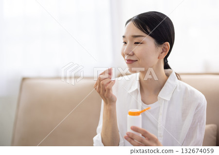 一位中年婦女將一片保健藥片放入口中 132674059
