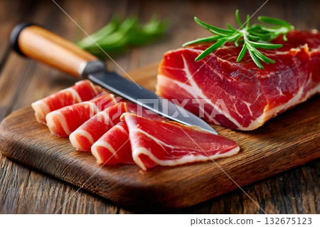Sliced cured ham with rosemary on wooden cutting board 132675123