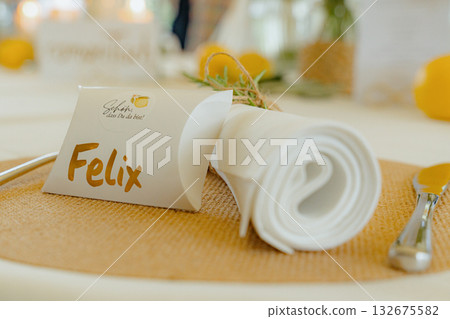 Personalized name card elegantly placed beside a neatly rolled napkin on a woven placemat, enhancing the sophisticated table setting atmosphere for a special event Personalized name card elegantly placed beside a neatly rolled napkin on a woven placemat, enhancing the sophisticated table setting atmosphere for a special event 132675582