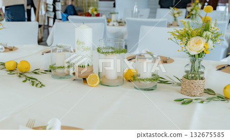 Wedding table adorned with candles, lemons, and floral arrangements creating an elegant atmosphere. Candles in glass holders and lemons complement the floral decor beautifully 132675585