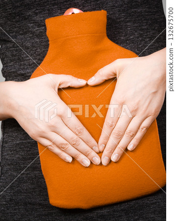 Girl holds hot water bottle on belly making heart shape by hands 132675700