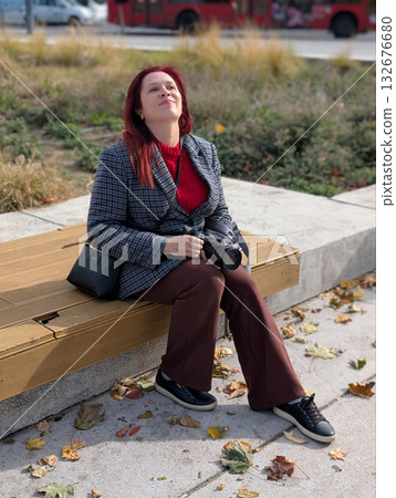 Woman sitting on bench holding camera on sunny day. Relaxation, creativity and inspiration through everyday outdoor lifestyle and photography passion. Woman sitting on bench holding camera on sunny day. Relaxation, creativity and inspiration through everyday outdoor lifestyle and photography passion. 132676680