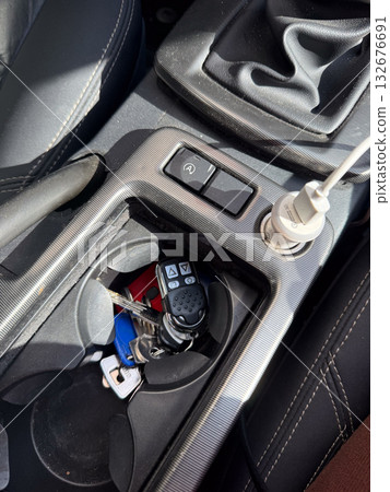 Car interior with car keys and remote in cup holder. Everyday life, transportation routine and personal mobility symbolized through driver essentials. Car interior with car keys and remote in cup holder. Everyday life, transportation routine and personal mobility symbolized through driver essentials. 132676691
