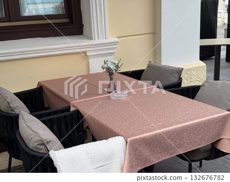 Outdoor cafe table with pink tablecloth and flower vase. Cozy urban terrace, relaxation, and street dining ambiance. Outdoor cafe table with pink tablecloth and flower vase. Cozy urban terrace, relaxation, and street dining ambiance. 132676782