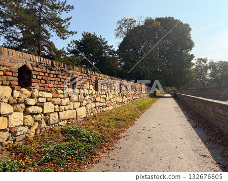 Stone wall and pathway in autumn park. Historical architecture, seasonal atmosphere, and tranquil outdoor perspective. Stone wall and pathway in autumn park. Historical architecture, seasonal atmosphere, and tranquil outdoor perspective. 132676805