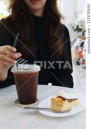 Female drinking iced coffees and a slice of cake on a table, blurred background. Female drinking iced coffees and a slice of cake on a table, blurred background. 132676848