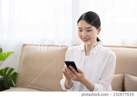 一位中年婦女坐在沙發上操作智慧型手機 132677019