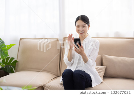 一位中年婦女坐在沙發上，正用智慧型手機進行視訊通話。 132677021