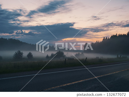 Early morning fog rolls across a field in rural near a two lane road Early morning fog rolls across a field in rural near a two lane road 132677072