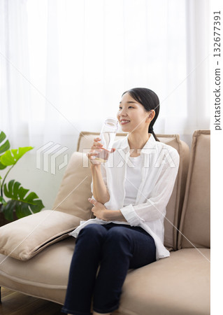 一位中年婦女坐在沙發上，帶著微笑，手裡拿著一瓶水。 132677391