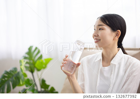 一位中年婦女坐在沙發上，帶著微笑，手裡拿著一瓶水。 132677392