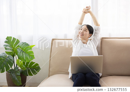 A middle-aged woman stretching on the sofa with a laptop computer on her lap and a smile 132677555
