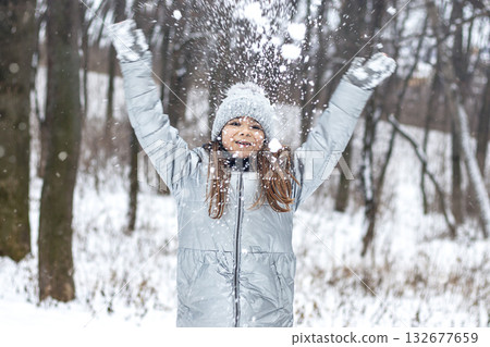 Girl in winter coat throws snow in the forest, joyful outdoor play scene for stock 132677659