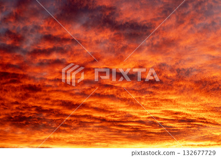 Fiery sunset paints dramatic sky with orange and red clouds over calm horizon Fiery sunset paints dramatic sky with orange and red clouds over calm horizon 132677729