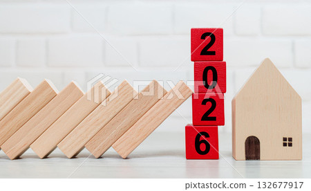 Red 2026 Wooden Blocks Standing Strong with House Model as Domino Blocks Collapse in Background 132677917