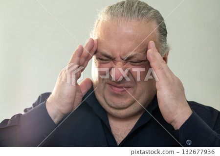 Man with headache holding temples in frustration and stress, showing fatigue and tension Man with headache holding temples in frustration and stress, showing fatigue and tension 132677936