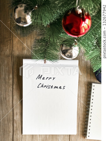 Merry Christmas is handwritten on the paper, and next to it is a Christmas tree with toys Merry Christmas is handwritten on the paper, and next to it is a Christmas tree with toys 132677942