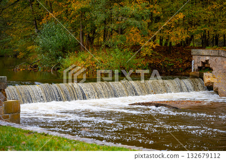 Viktorka Weir flows gracefully in Granny Walley, Ratiborice, surrounded by colorful trees and serene nature. It captures the peaceful essence of rural life and literature. 132679112