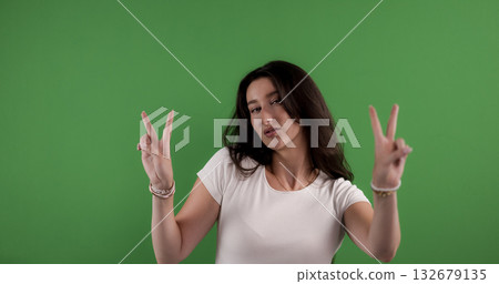 Young woman making peace sign with both hands on green background Young woman making peace sign with both hands on green background 132679135