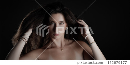 Fashion model playing with her long brown hair on black background Fashion model playing with her long brown hair on black background 132679177