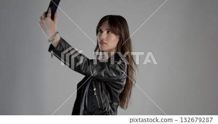 Fashion model taking selfie with smartphone wearing black leather jacket Fashion model taking selfie with smartphone wearing black leather jacket 132679287