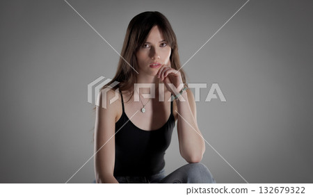 Fashion model posing with hand on chin, wearing black top and jeans Fashion model posing with hand on chin, wearing black top and jeans 132679322