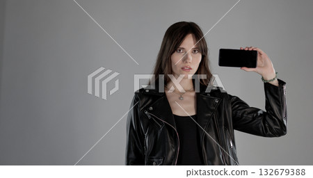 Fashion model showing smartphone with blank screen wearing black leather jacket 132679388