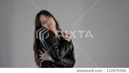 Fashion model wearing black leather jacket hugging herself with closed eyes 132679390