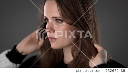 Beautiful young woman playing with her hair on gray background Beautiful young woman playing with her hair on gray background 132679486