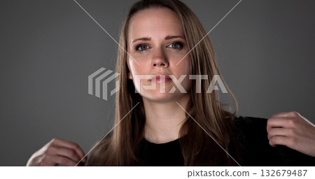 Serious young woman adjusting black sweater on gray background Serious young woman adjusting black sweater on gray background 132679487