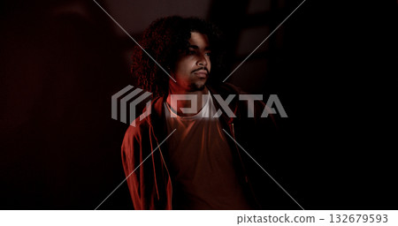 Young african-american man with curly hair looking away in dark room with red light 132679593
