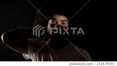 Young african-american man with curly hair posing in the shadows with hand behind neck Young african-american man with curly hair posing in the shadows with hand behind neck 132679595