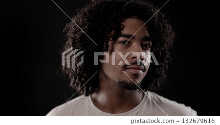 Young african-american man with curly hair posing on dark background Young african-american man with curly hair posing on dark background 132679616