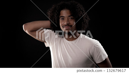 Young african-american man with curly hair touching his head and smiling on black background Young african-american man with curly hair touching his head and smiling on black background 132679617