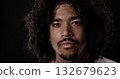 Portrait of a serious young african-american man with curly hair and goatee looking intensely against a black background 132679623