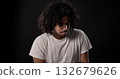 Young african-american man with curly hair looking down and thinking against black background 132679626