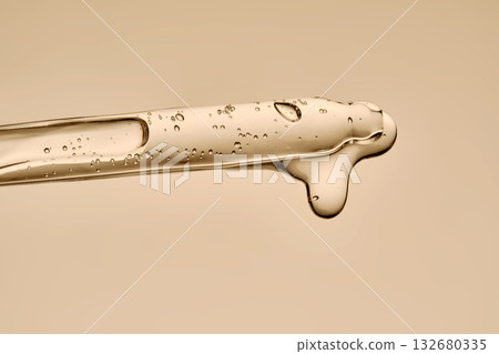 The texture of the serum flowing out of the pipette on a beige background. The texture of the serum flowing out of the pipette on a beige background. 132680335