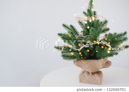 Small decorated christmas tree with burlap base and fairy lights on white background 132680701